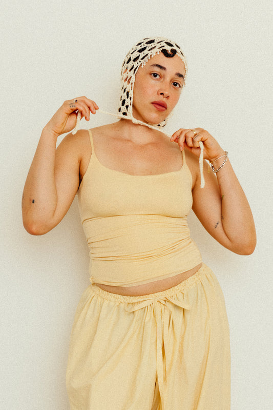 Woman wearing a butter yellow top and pants with a crocheted head dress against a white background